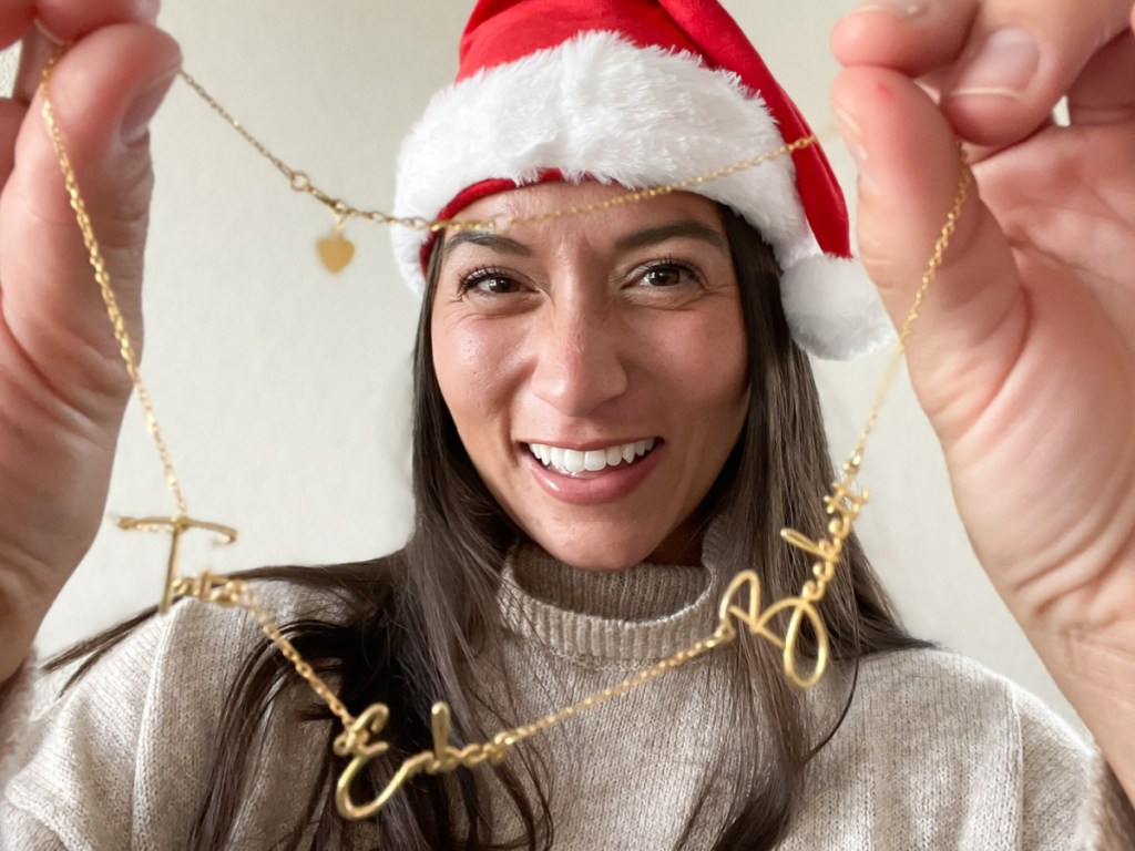 woman in santa hat holding up name necklace