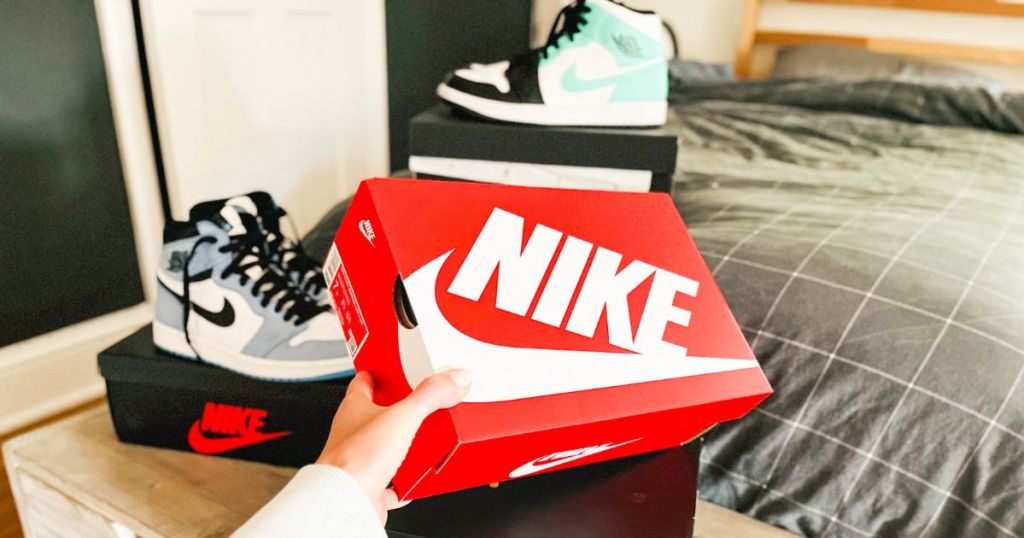 Person hält eine Nike-Box mit zwei Paar Air Jordans im Hintergrund