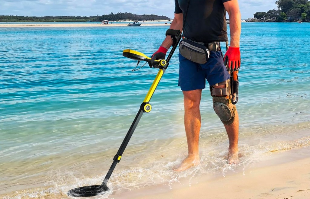 man holding yellow and black metal detector at beach