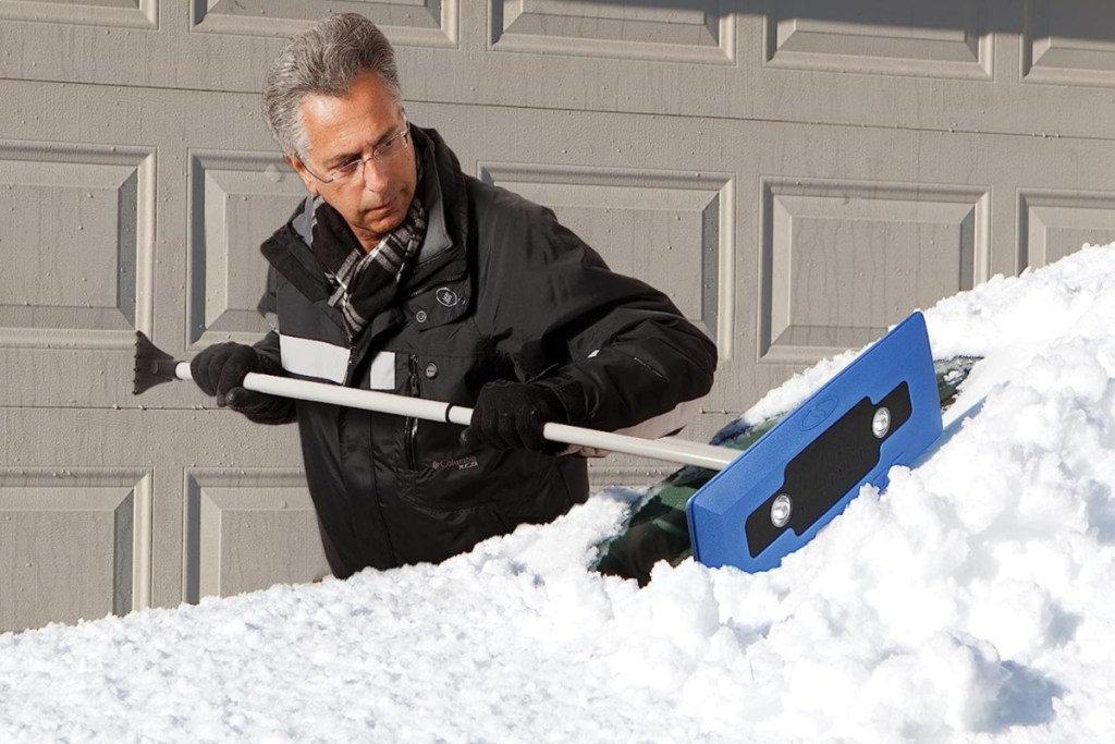 man using a snow joe snow broom to clean snow off of a car