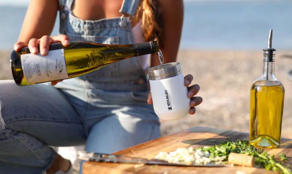 a woman ona beach pouring white wine into a white stanley Wine tumbler