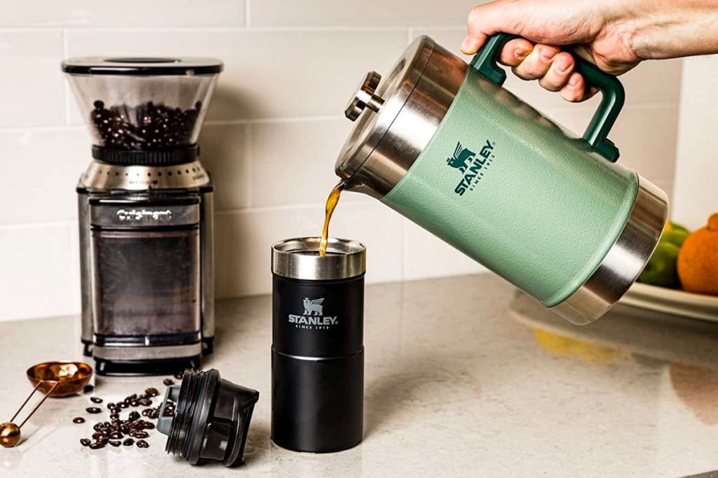 a woman's hand pouring coffee into an insulated travel mug from a stanley french press