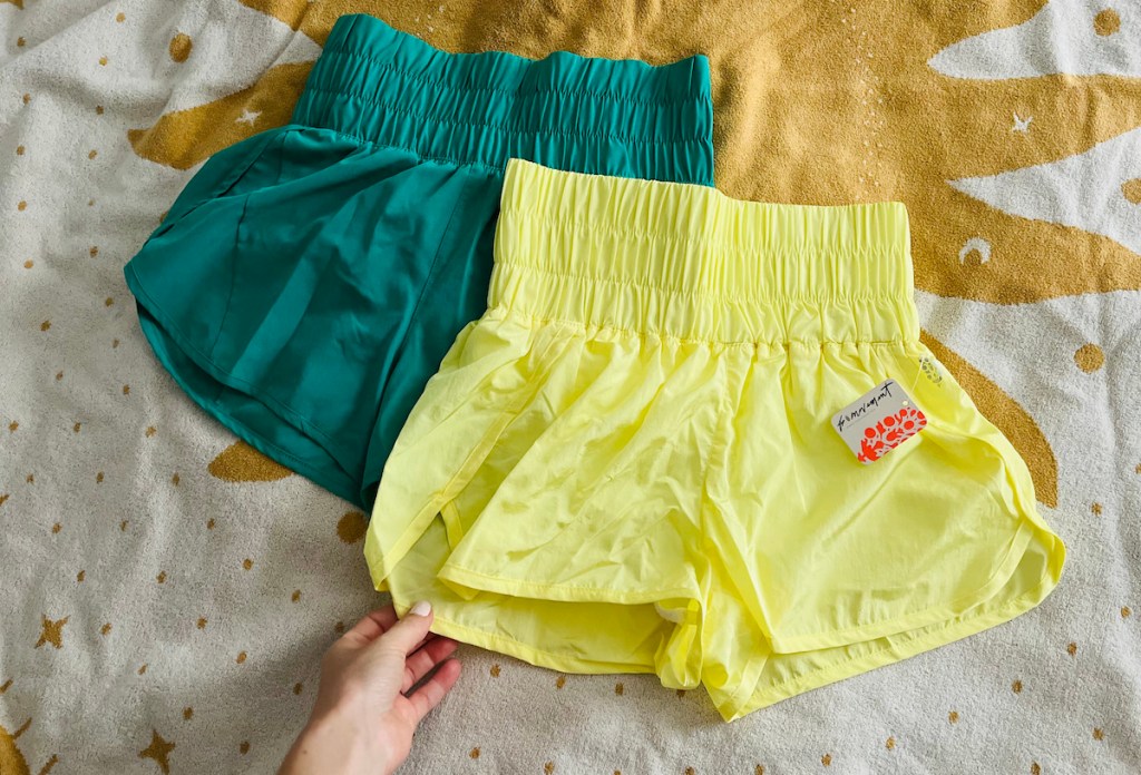 hand holding edge of yellow free people the way home shorts with avia shorts walmart underneath