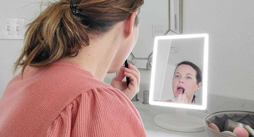 woman applying makeup using lighted mirror in front of her