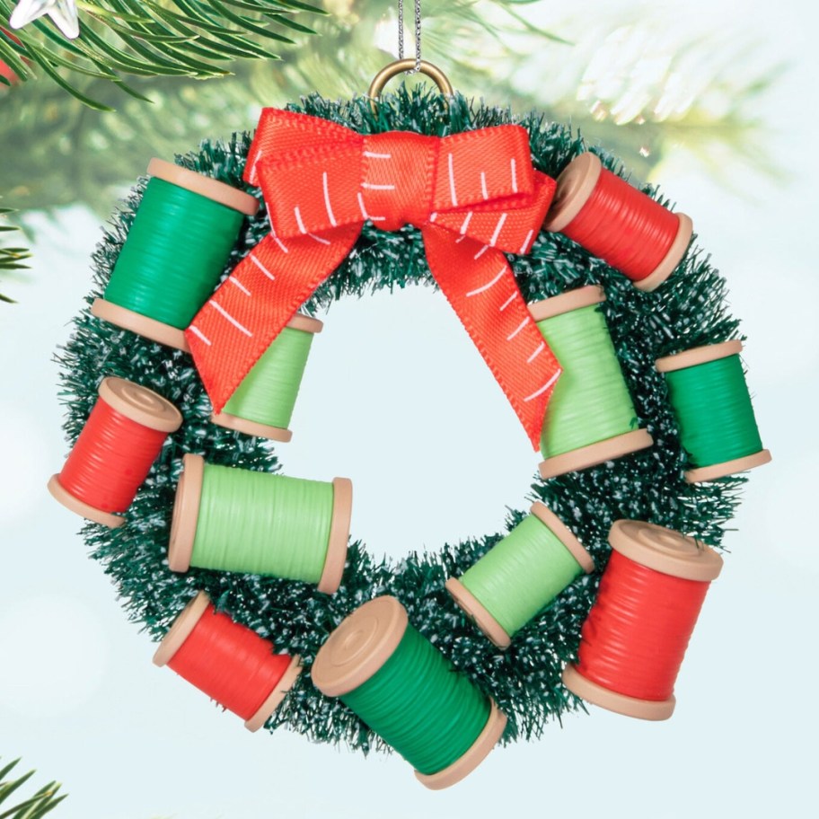 a wreath shaped Christmas ornament with bobbins of thread hanging from a tree limb