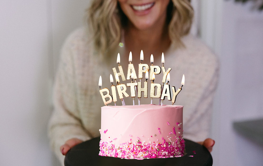 woman smiling holding plate with pink happy birthday cake