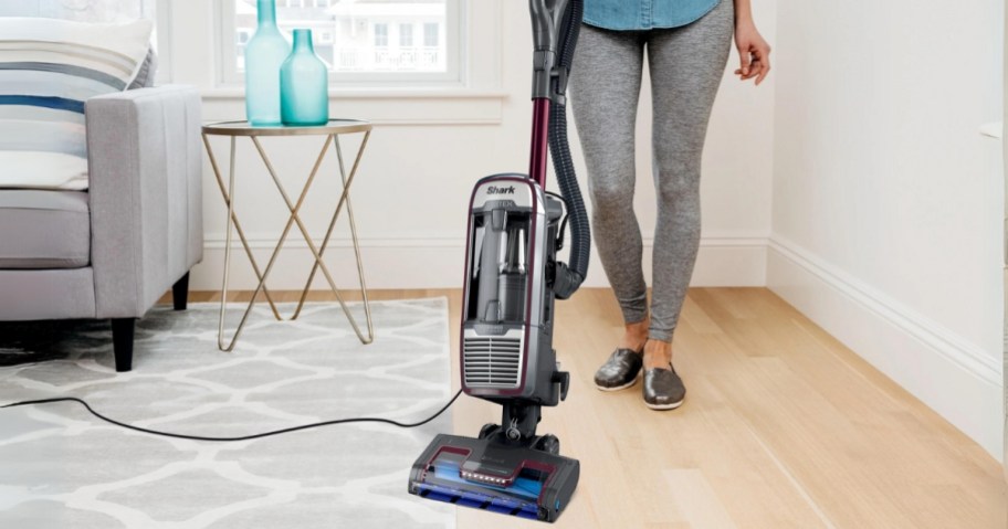 woman vacuuming a hardwood floor and carpet rug with a Shark vacuum cleaner