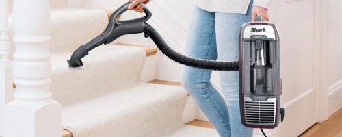 woman vacuuming carpeted stairs with a Shark Vacuum