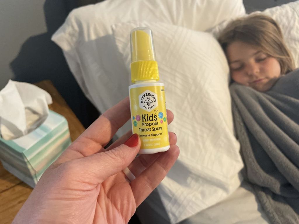 Woman holding Beekeeper's Naturals Kids Propolis Throat Spray 95% Bee Propolis Extract for a little girl who is laying down