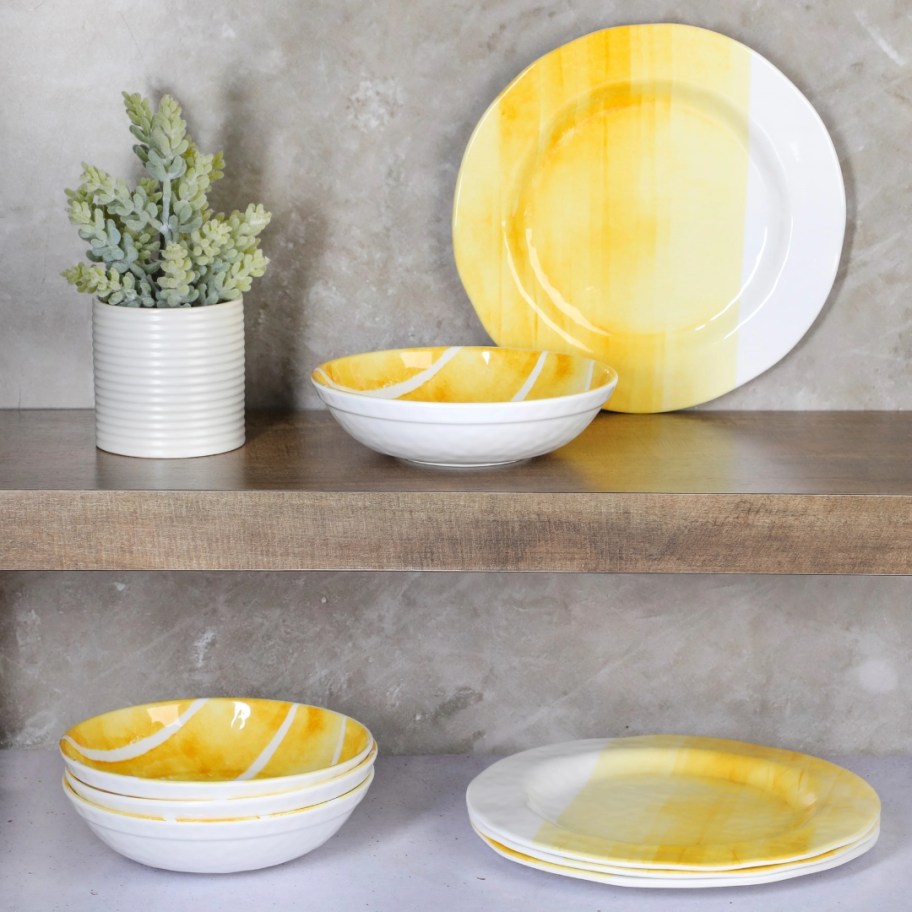 yellow and white watercolor style melamine dinner plates and bowls on a wood shelf and counter next to a plant