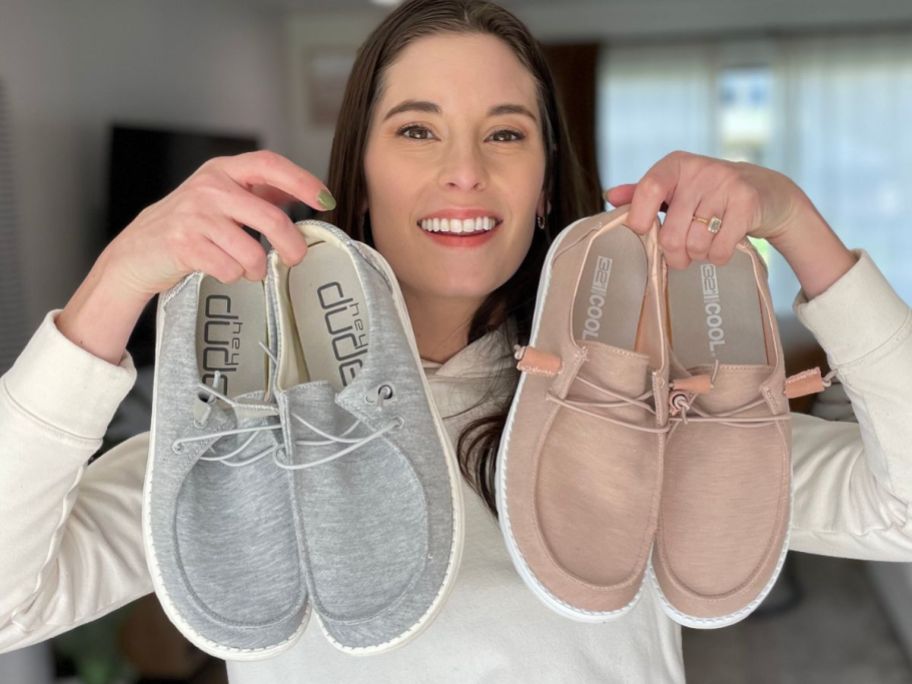 woman holding up a pair of 32 Degrees slip on shoes next to a pair of Hey Dude shoes