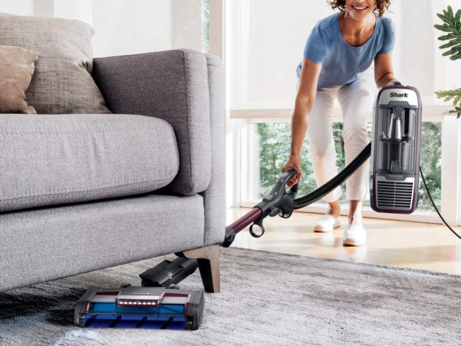 woman vacuuming under a couch with a Shark vacuum