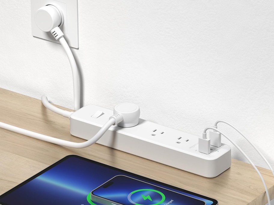 white power strip plugged into wall with tablet and phone plugged in and charging