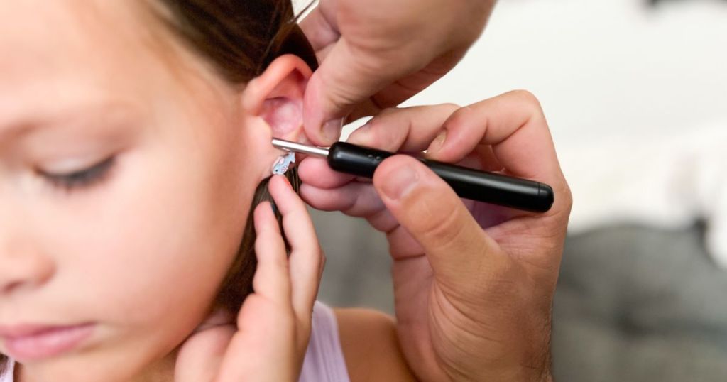 person putting ear removal wand in girls ear