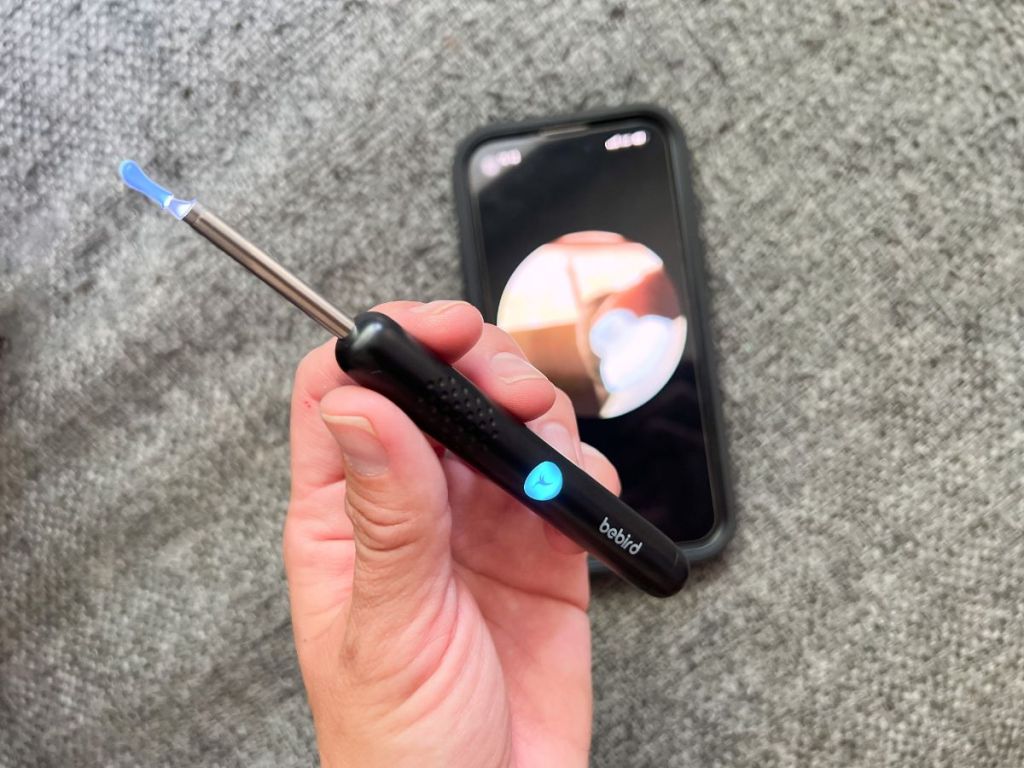 person holding ear removal wand near phone