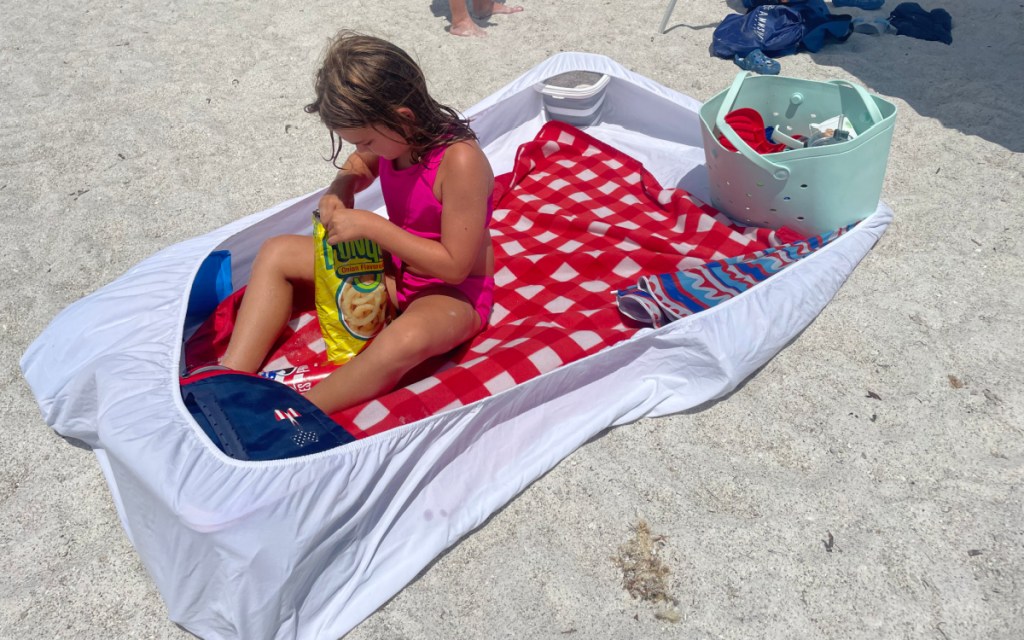 young girl at the beach using a clever beach hack to keep sand off her towel