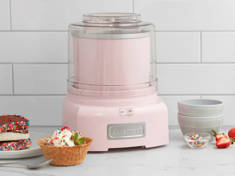 pink Cuisinart ice cream maker on a kitchen counter next to a bowl of ice cream and fruit
