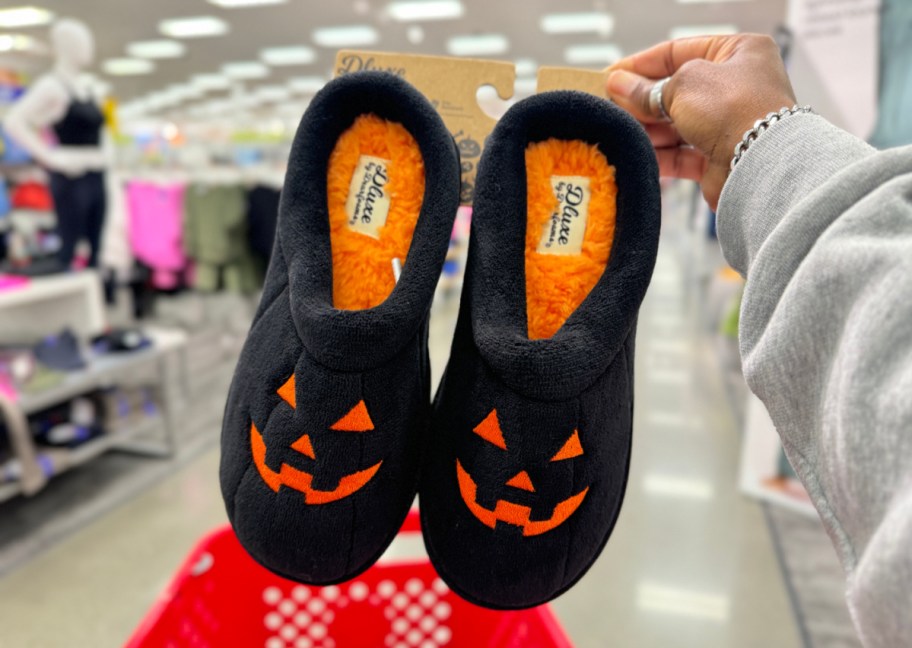 Hand holding Dearfoam Halloween Jack o lantern Slippers from Target