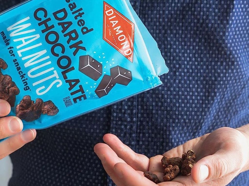 hand pouring Diamond of California Salted Dark Chocolate Walnuts from the bag into their other hand