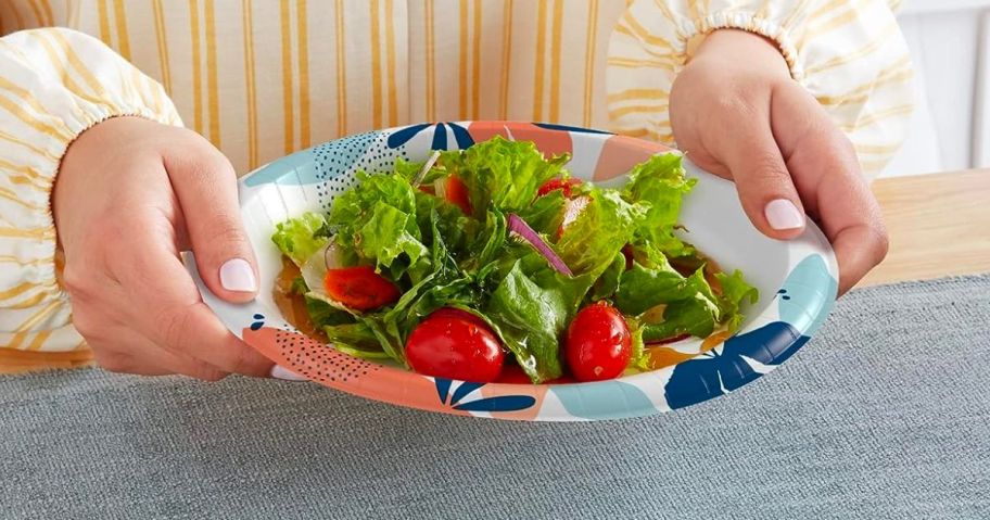 a woman holding a Dixie paper plate with salad on it