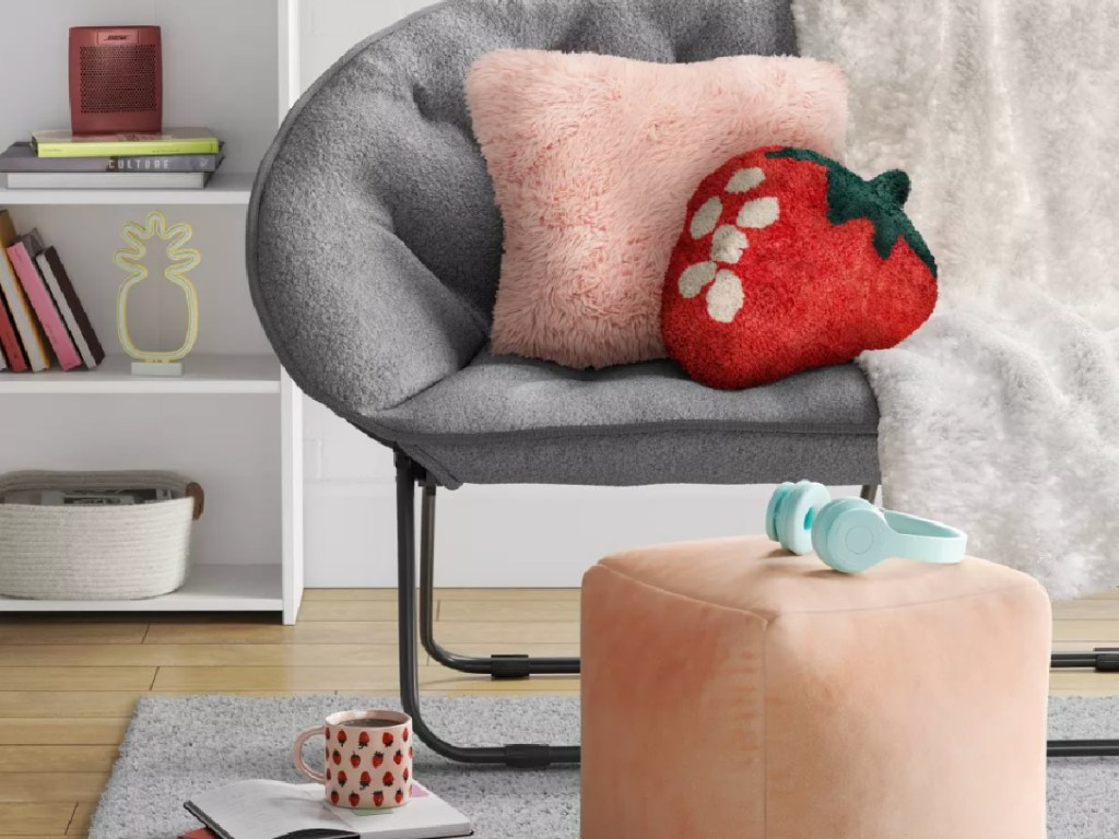 dorm room with gray chair, strawberry pillow, pink pouf and blue headphones