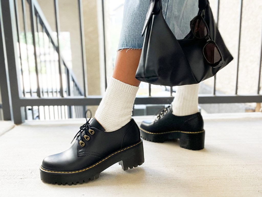 woman wearing a pair of black dr martens shoes with white socks and holding black bag 