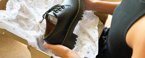 woman unboxing a pair of black leather dr martens shoes