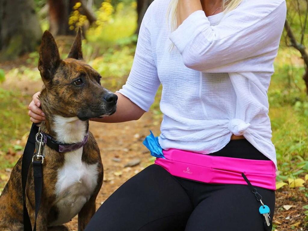 woman wearing a pink flipbelt kneeling on a trail next to a dog