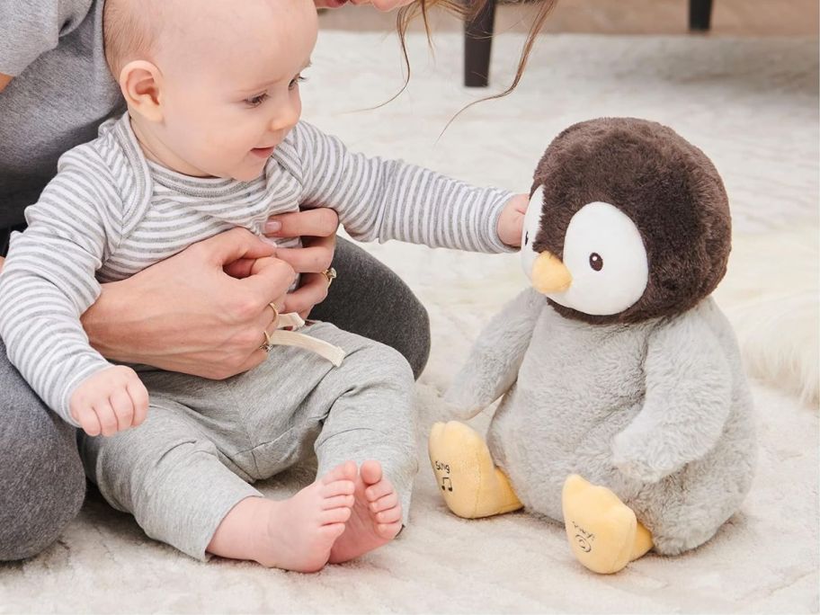 a baby playing with a singing penguin plush