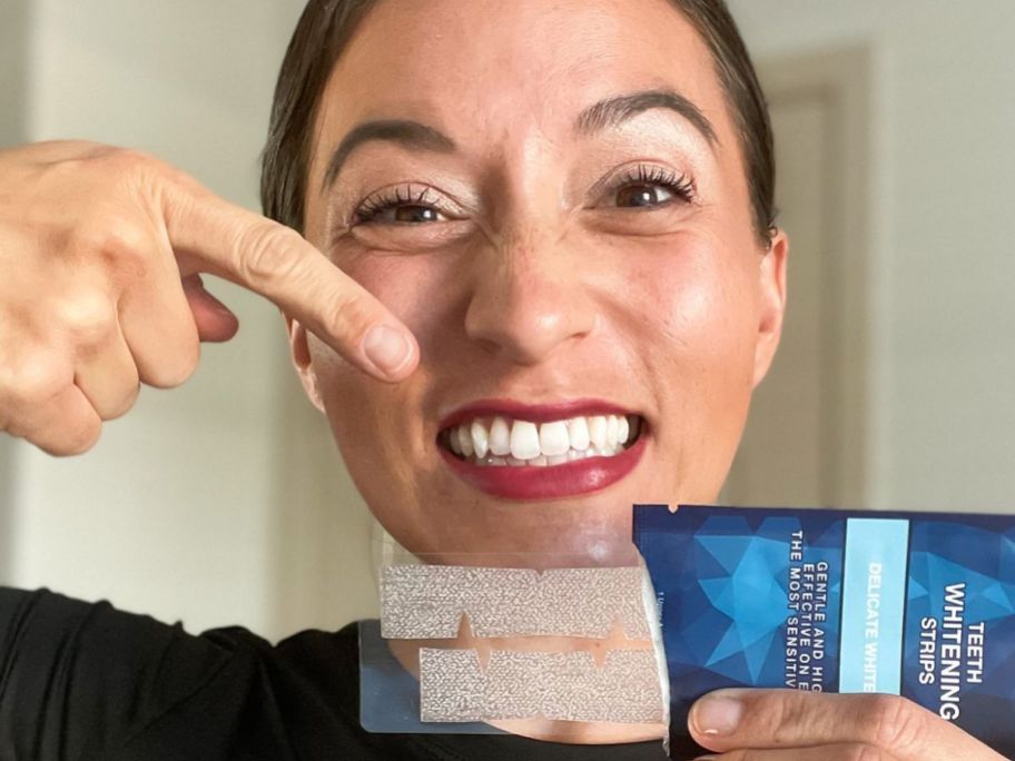 Woman pointing to tooth whitening trips while smiling ddisplay very white teeth