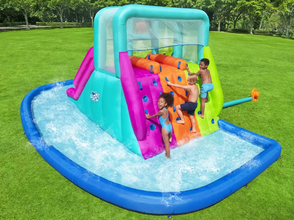 three kids climbing up inflatable water park