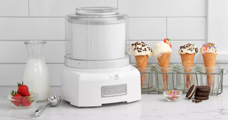 red Cuisinart ice cream maker on a kitchen counter next to a set of ice cream cones with ice cream and different toppings