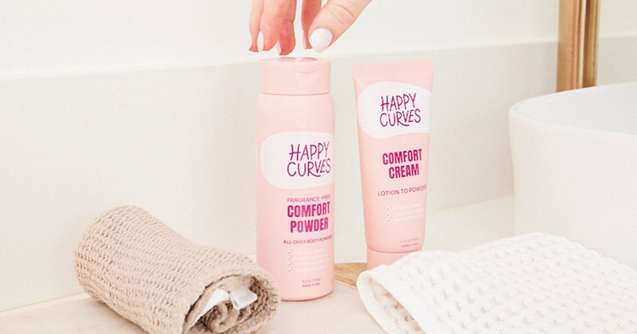 hand grabbing a pink bottle of Happy Curves Comfort Powder
