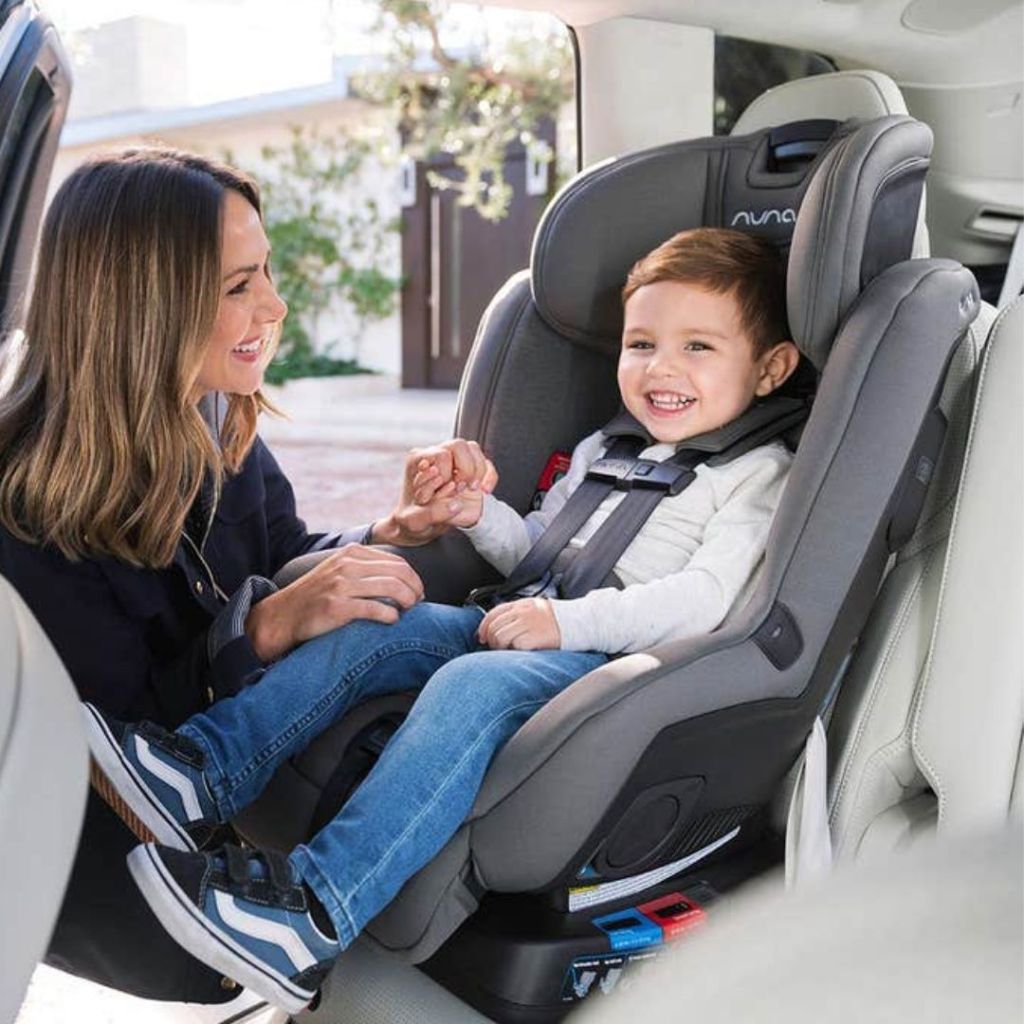 RAVA™ Flame Retardant Free Convertible Car Seat shown with a toddler age boy sitting and mom buckling him in