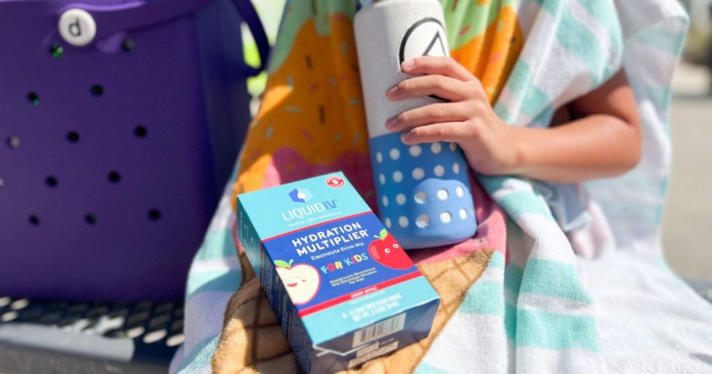 LiquidIV Hydration Multiplier for Kids in Crisp Apple shown with a kid drinking out of a water bottle, wrapped in a beach towel by the pool