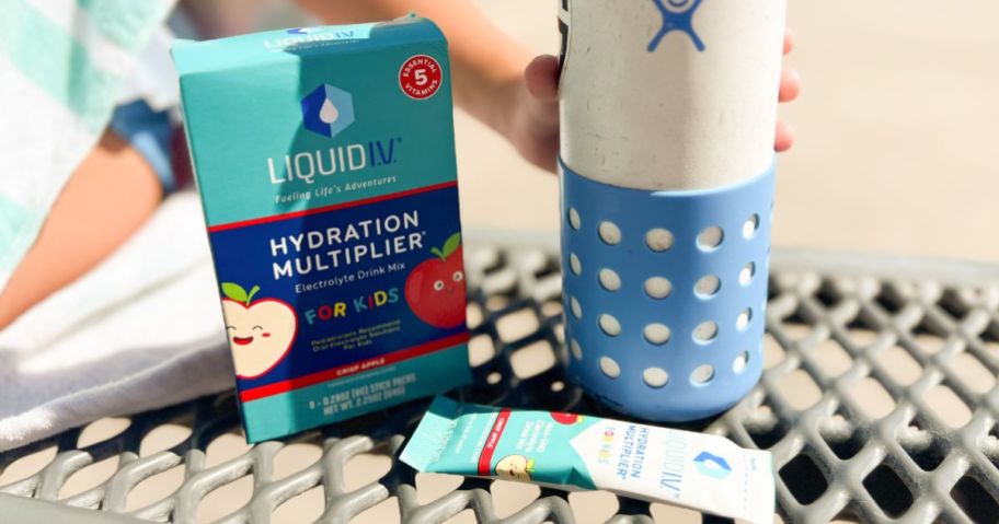 LiquidIV Hydration Multiplier for Kids in Crisp Apple, box and packet shown on bench with water battle by the pool