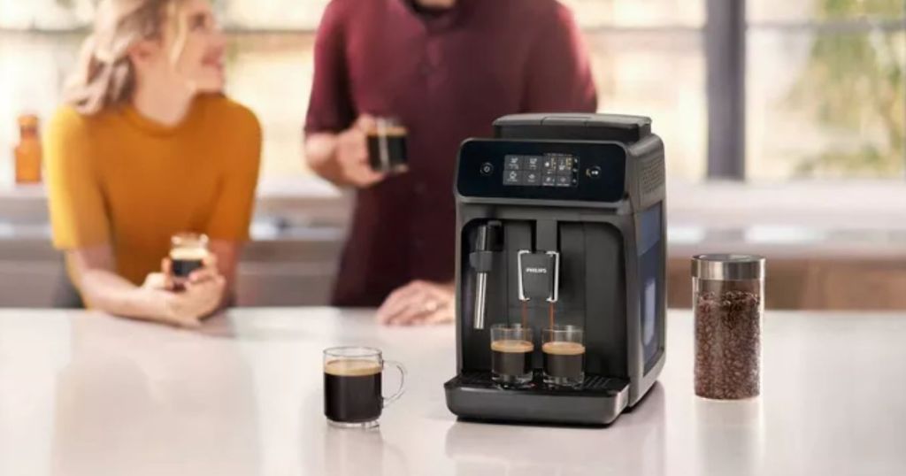 Paar trinkt Espresso an einer Theke hinter einer vollautomatischen Espressomaschine der Serie 1200 von Philips mit Milchaufschäumer