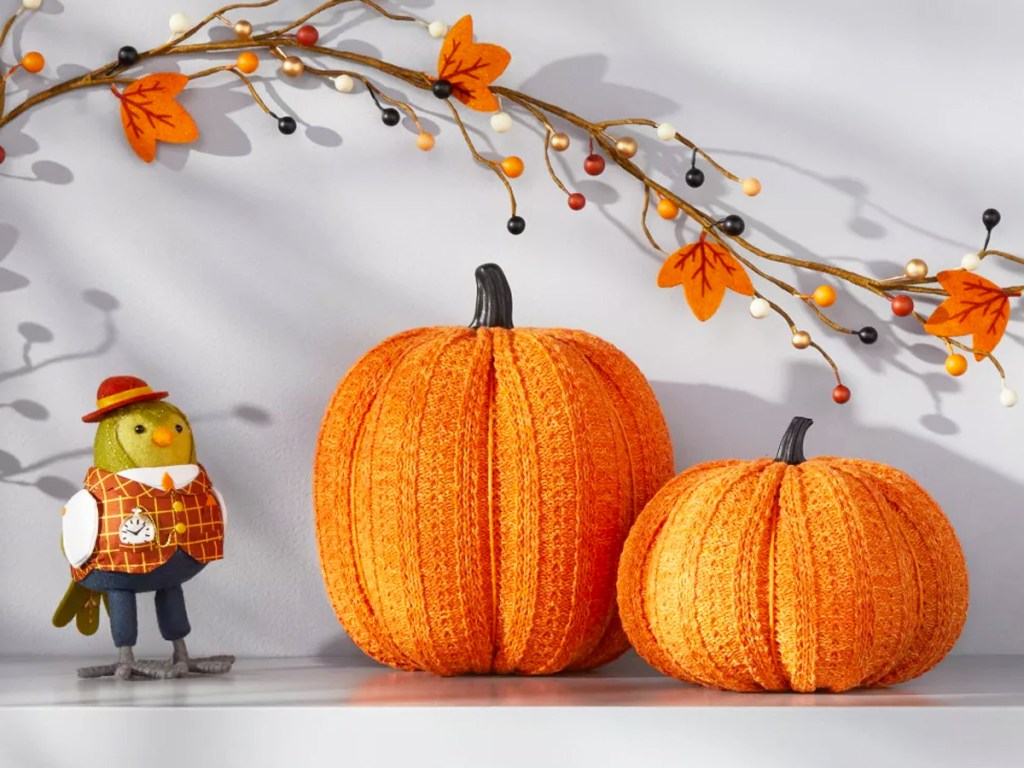two orange knit pumpkins next to autumn bird figure