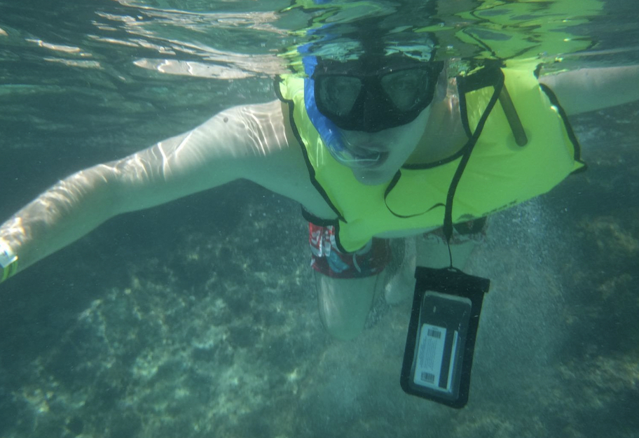 man snorkeling under water with waterproof phone case hanging from neck