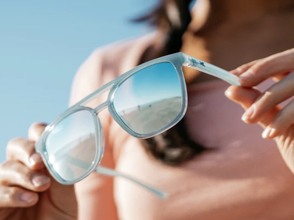 woman holding a pair of light blue sunglasses