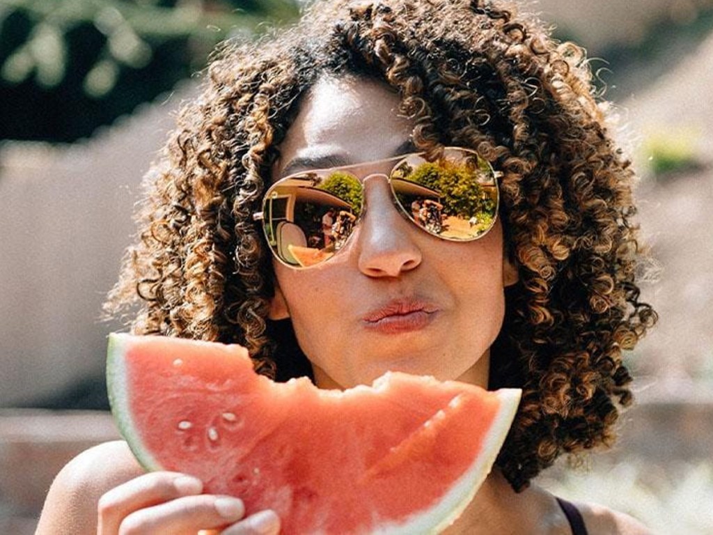 woman wearing sunglasses eating slice of watermelon