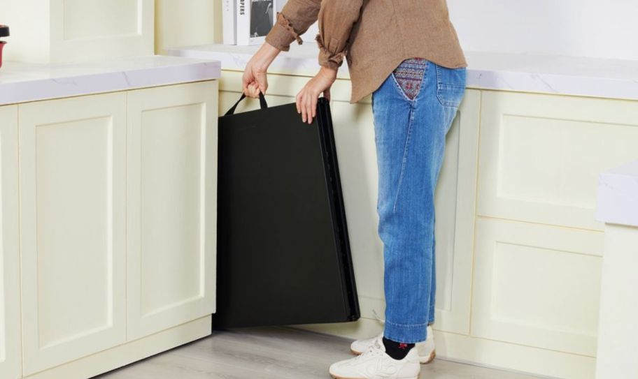 a woman storing a plastic folding table in a kitchen