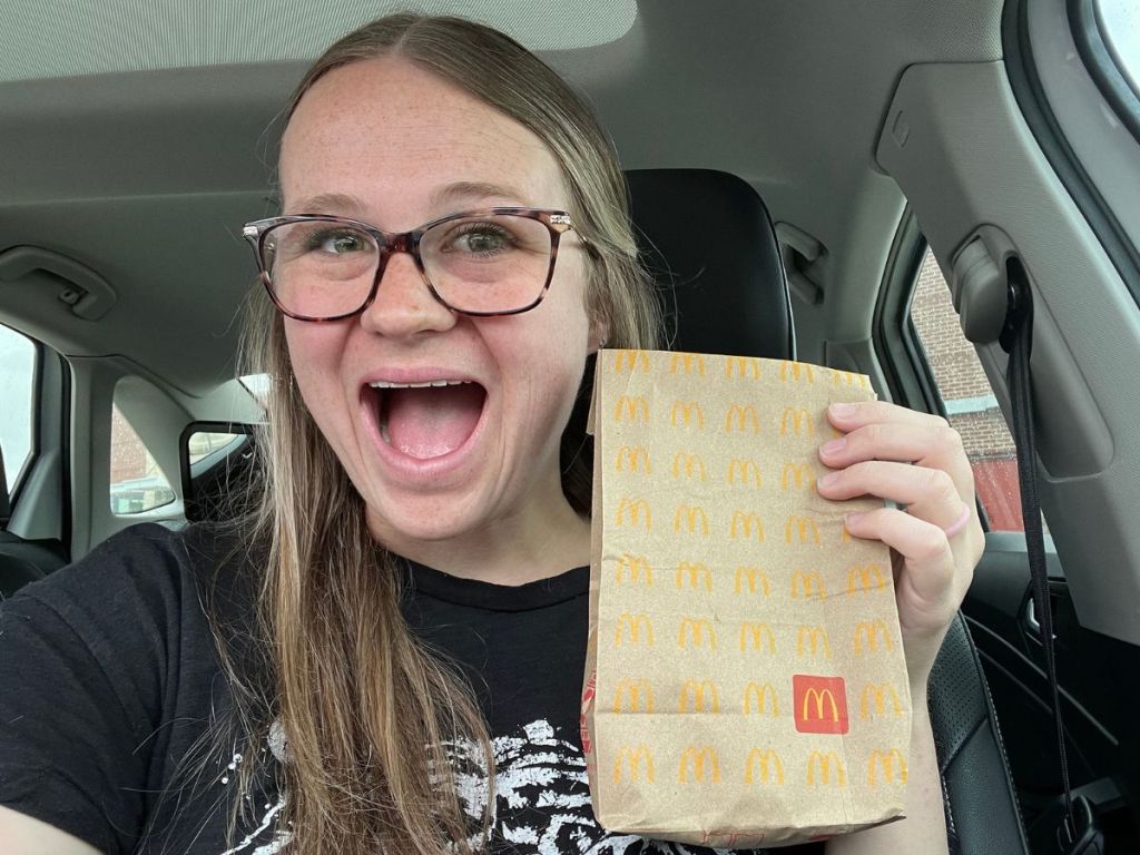 woman holding a mcDonalds bag with a very excited look on her face