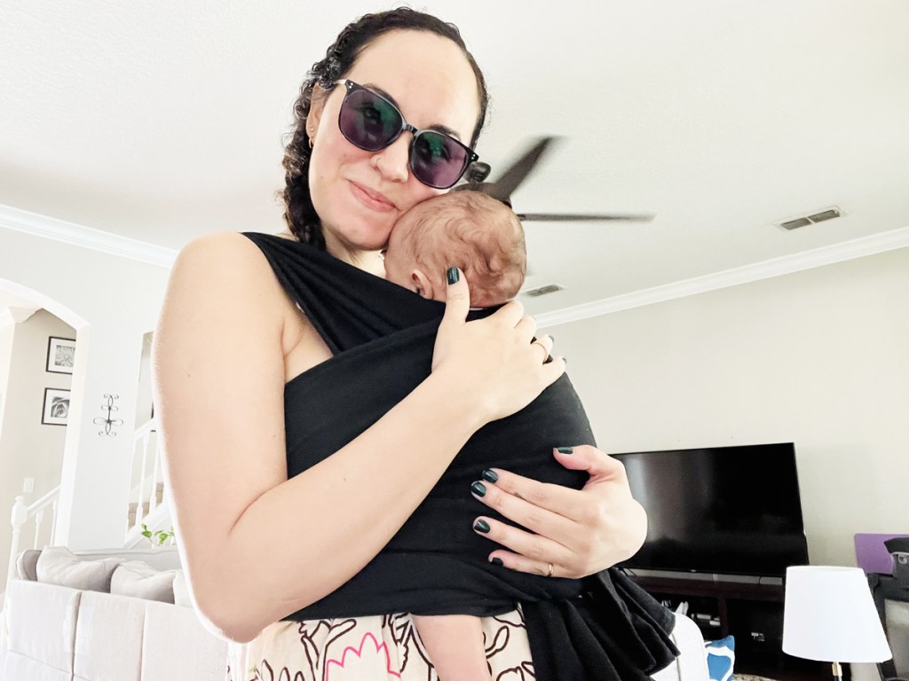 woman hugging baby in black carrier sling on her chest