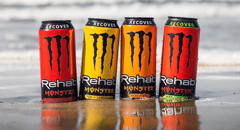 4 Monster Rehab cans on a beach