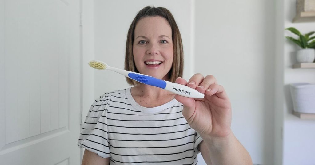 woman holding up Mouthwatchers Doctor Plotkas Extra Soft Flossing Toothbrush in front of her face