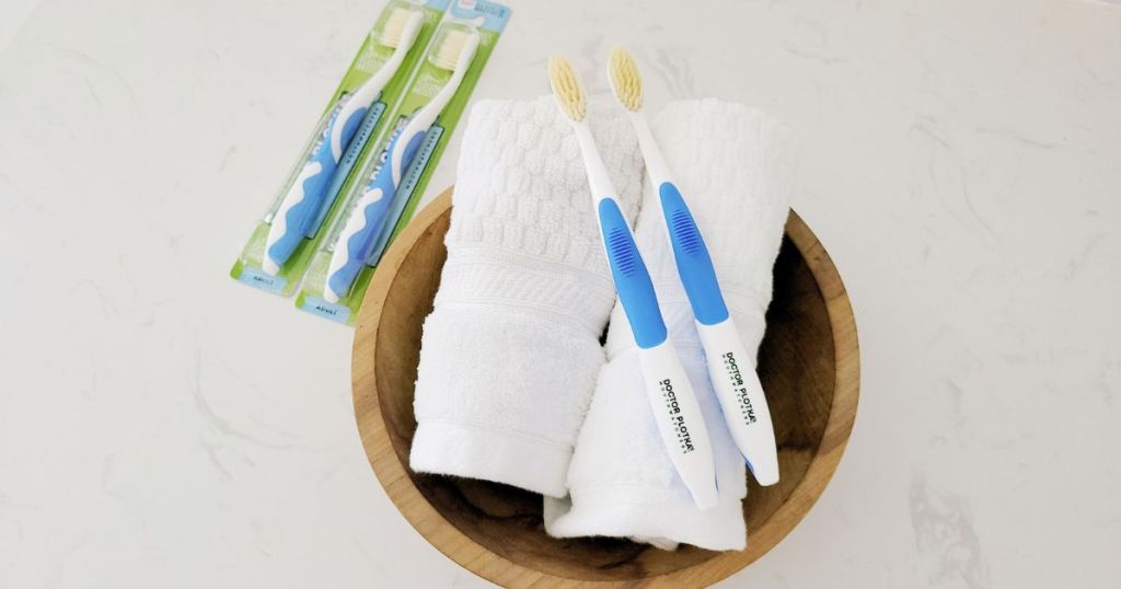 2 Doctor Plotkas Extra Soft Flossing Toothbrushes resting on towes in bowl next to 2 toothbrushes still in the package
