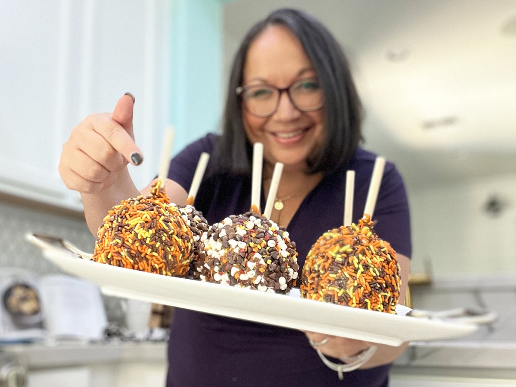 woman holding a tray of sprinkle covered caramel apples