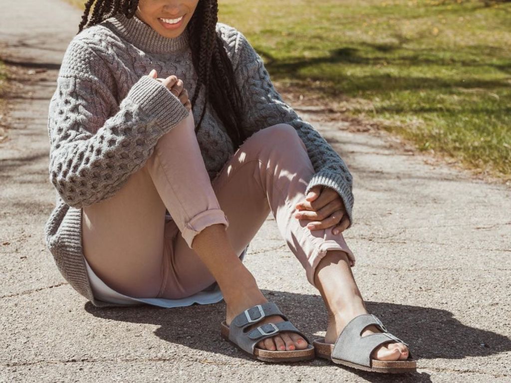 woman sitting on the ground wearing Muk Luks marla sandals