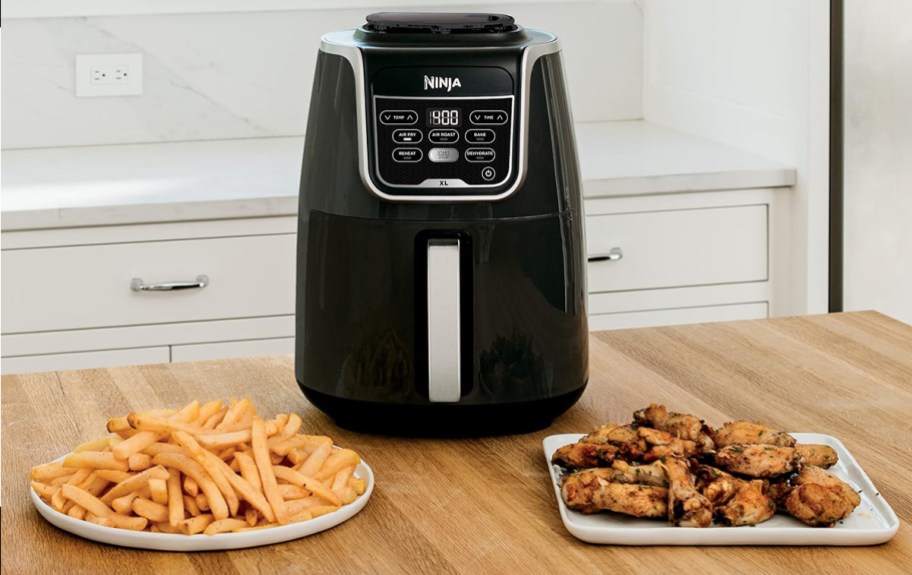 ninja air fryer sitting on a table with a plate of fries and chicken wings